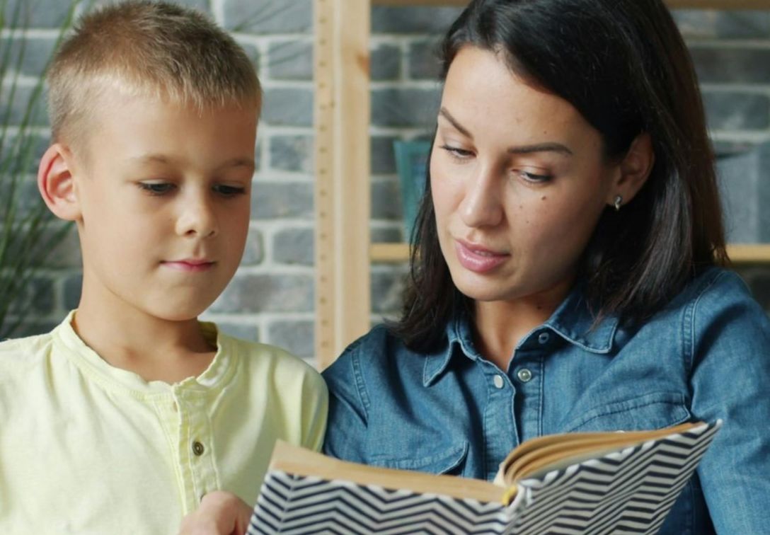 Um adulto acompanha uma criança na leitura de um livro, orientando e apoiando a compreensão passo a passo. Esta estratégia é frequentemente utilizada na dislexia, promovendo a leitura guiada, o reforço da associação entre sons e letras e o aumento da confiança na interpretação do texto.