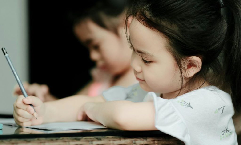 Uma criança escreve com esforço e concentração, evidenciando dificuldades na escrita que podem afetar a precisão, a fluidez e a organização no papel.