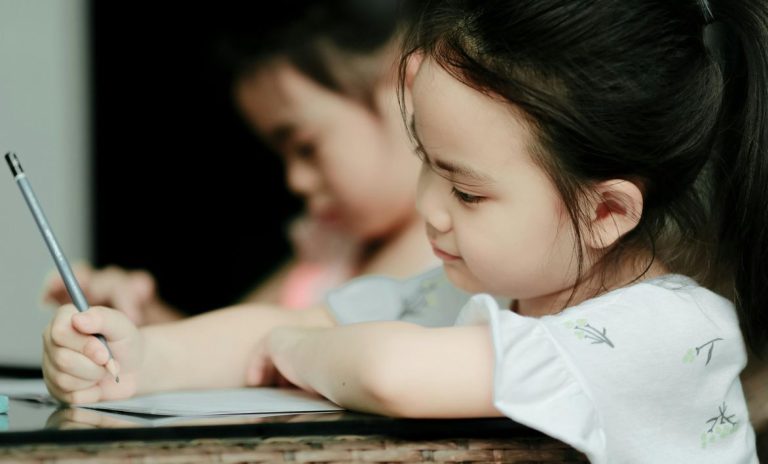 Uma criança escreve com esforço e concentração, evidenciando dificuldades na escrita que podem afetar a precisão, a fluidez e a organização no papel.