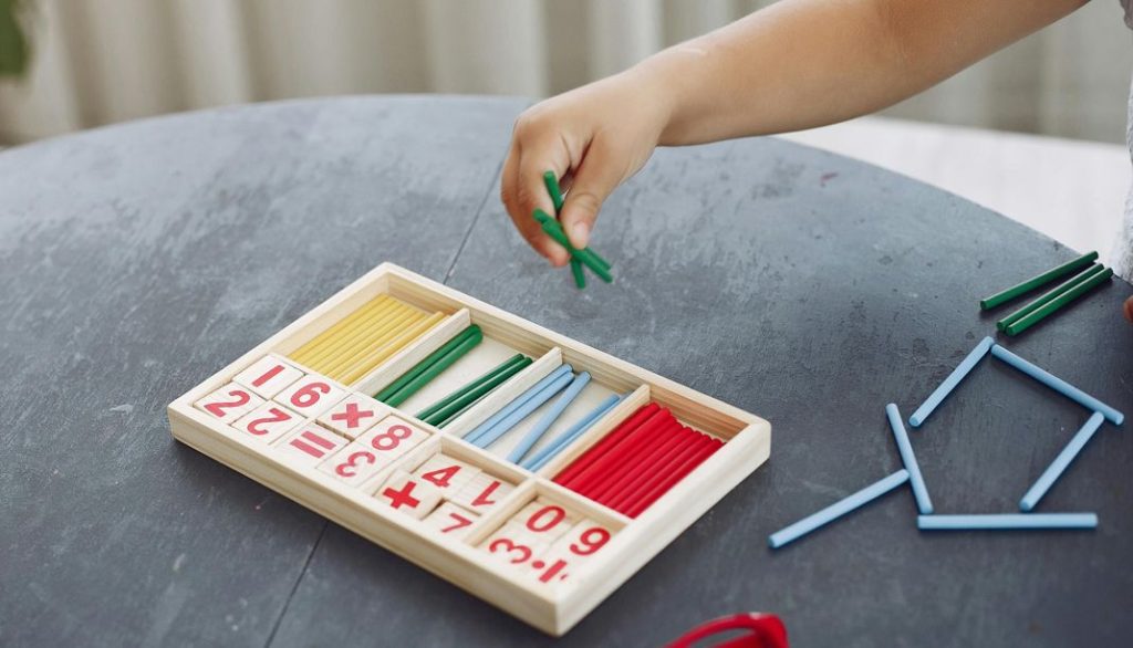 Uma criança utiliza peças coloridas para contar, explorando números de forma prática e visual, o que facilita a compreensão das quantidades e o desenvolvimento do raciocínio matemático.