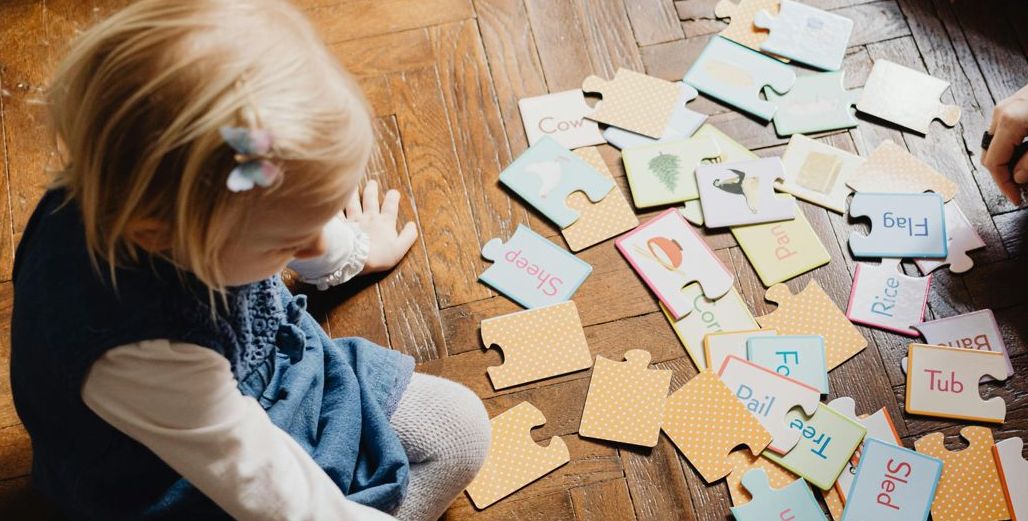 Uma criança explora peças de puzzle com palavras e imagens, utilizando uma estratégia lúdica que estimula a associação, o reconhecimento visual e o desenvolvimento da linguagem de forma natural.