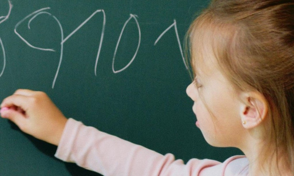 Uma criança escreve no quadro com alguma imprecisão, evidenciando dificuldades típicas das dificuldades de aprendizagem, que afetam a organização e a expressão da informação.