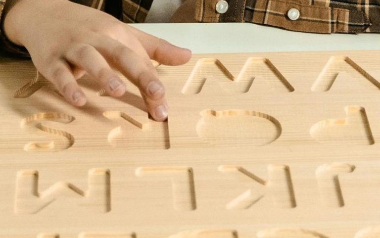 Uma criança explora letras num suporte de madeira, evidenciando dificuldades típicas da dislexia, que afetam o reconhecimento e a organização da informação escrita.