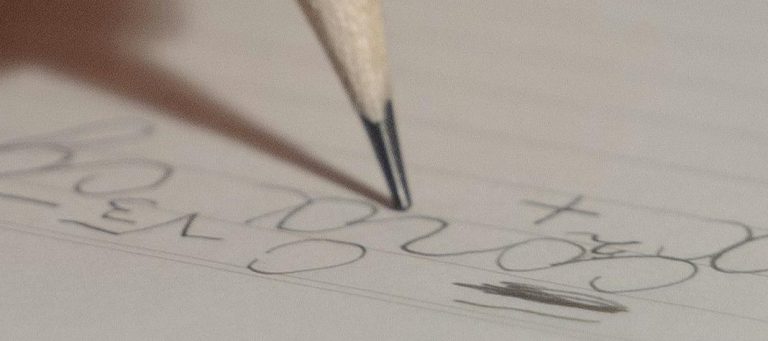 Um lápis escreve números e símbolos no papel, com traços irregulares e pouco consistentes, evidenciando dificuldade no controlo do movimento e na organização gráfica. A escrita apresenta variações no tamanho, alinhamento instável e pressão desigual, aspetos frequentemente associados à disgrafia. Este tipo de dificuldade pode refletir desafios na coordenação motora fina, no planeamento motor e na organização visuoespacial, interferindo na legibilidade e na fluidez da escrita.